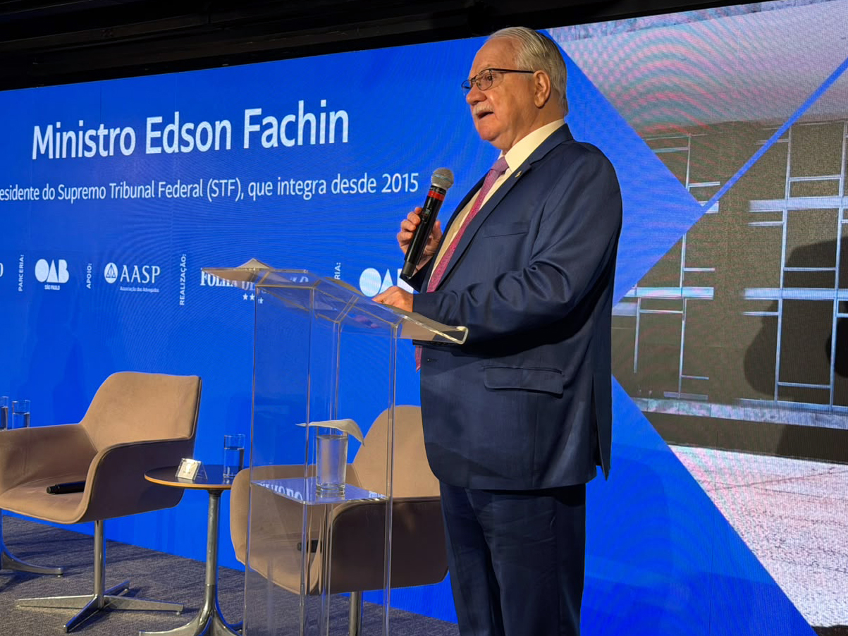 Ministro Edson Fachin discursa em um evento com backdrop informativo ao fundo.
