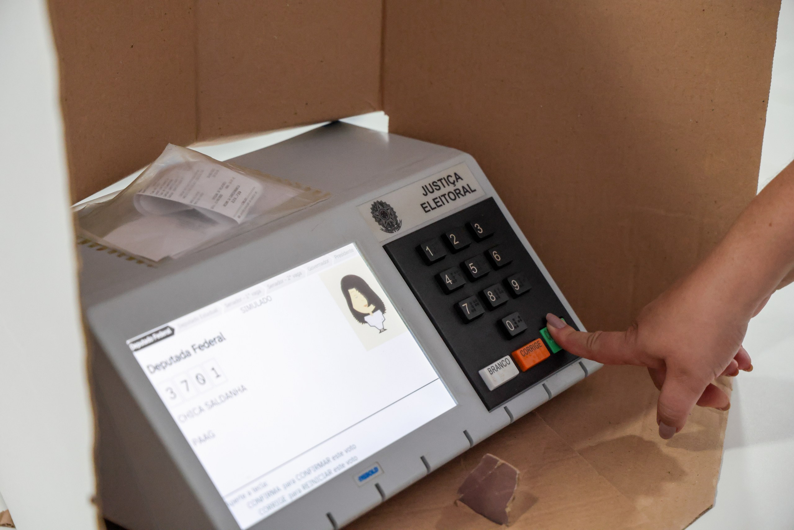 Close-up de uma mão operando uma urna eletrônica da Justiça Eleitoral durante um processo de votação.