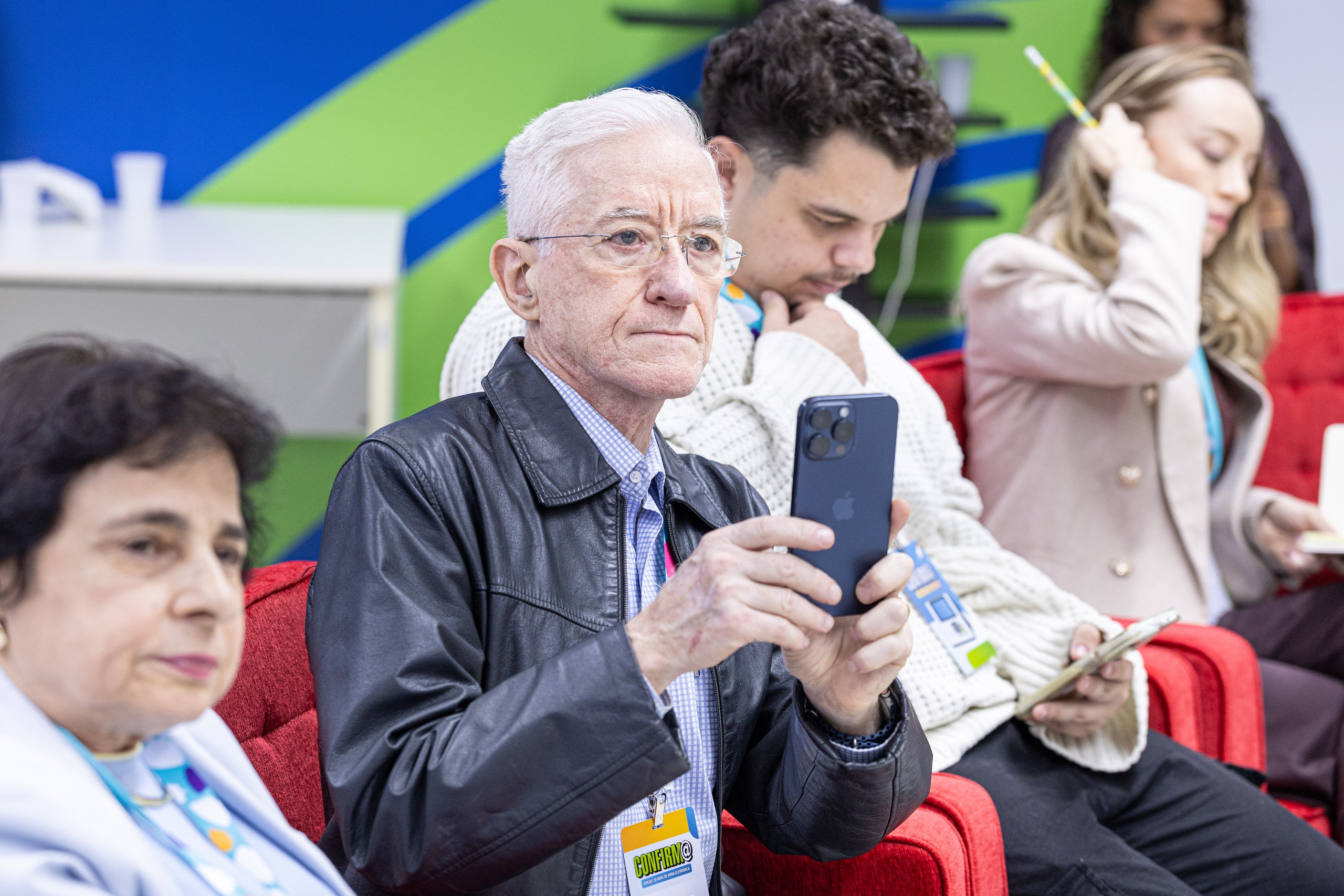 Um grupo de pessoas assiste a um evento, com um homem em destaque utilizando um smartphone.