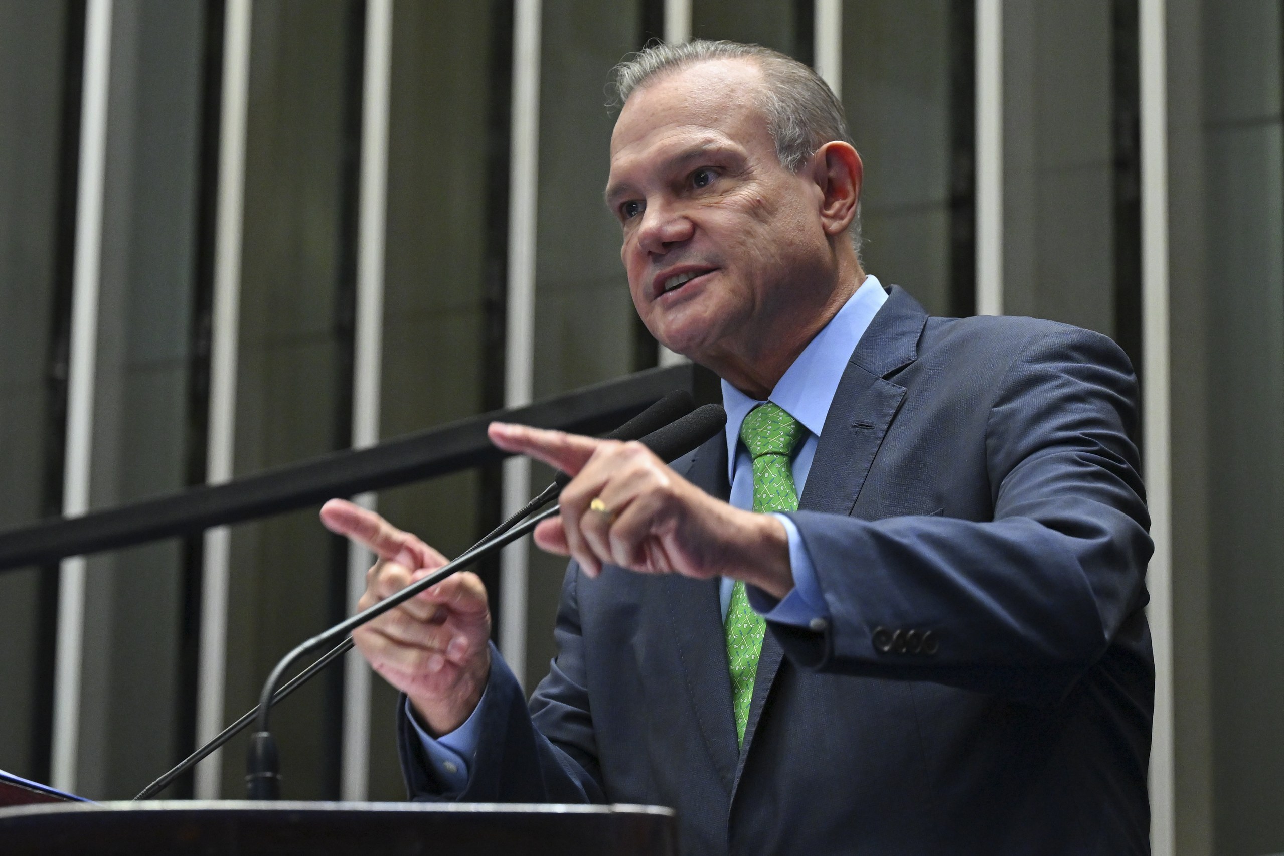 Homem de terno e gravata verde discursando em um púlpito.