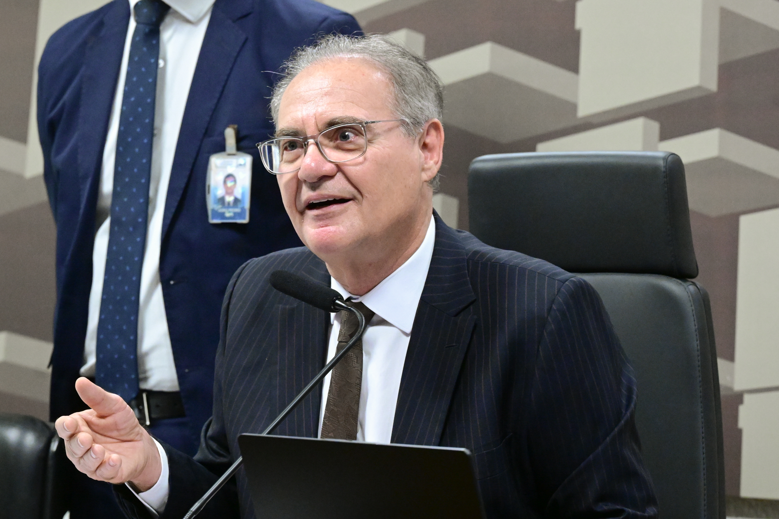 Homem de terno e óculos fala ao microfone em ambiente formal. Na foto: Renan Calheiros.