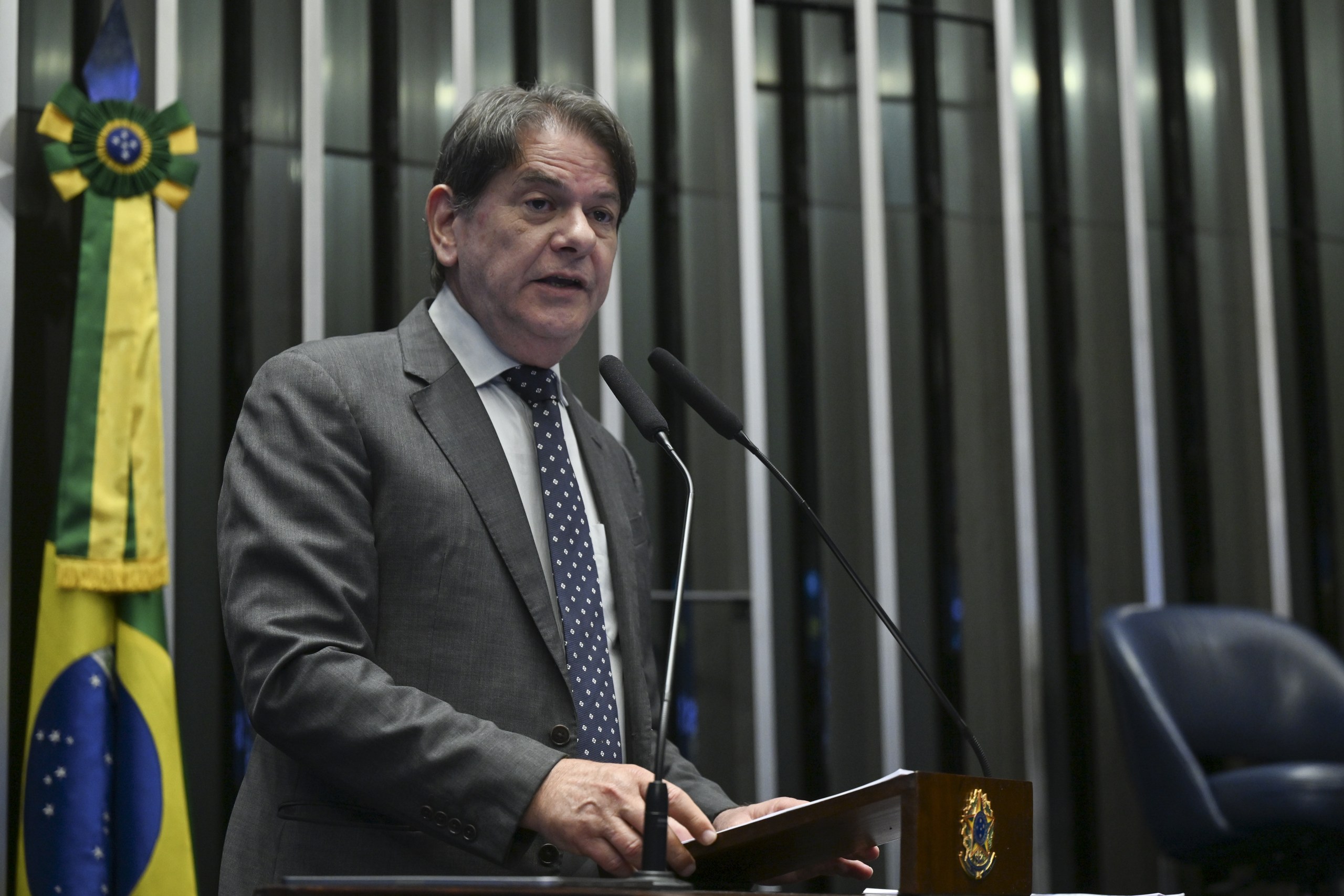 Um homem de terno e gravata fala ao microfone em um púlpito de madeira, com a bandeira do Brasil ao fundo. Na foto: Cid Gomes.