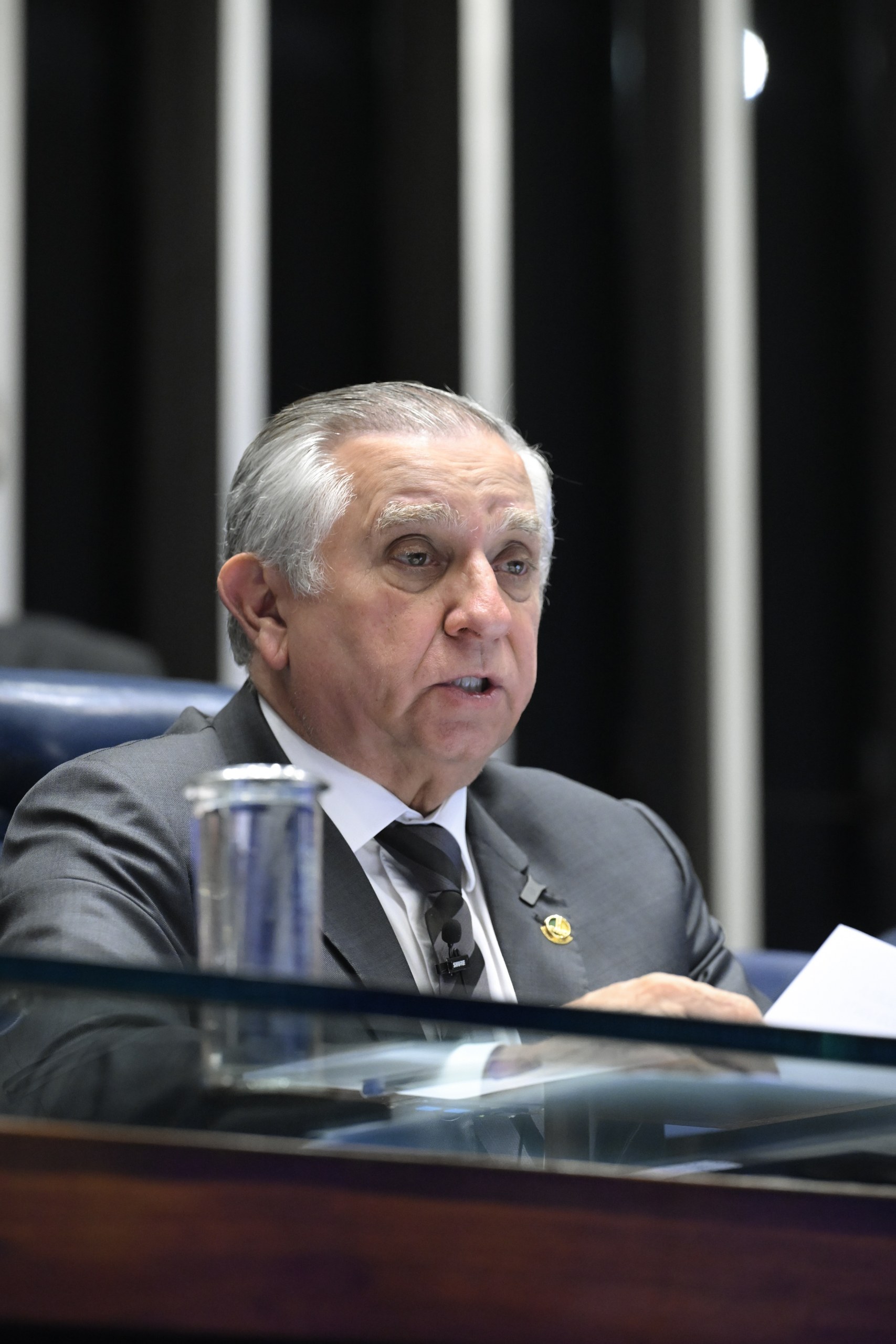 Um homem de terno e gravata fala durante sessão em ambiente formal, com papéis sobre a mesa à sua frente. Na foto: Izalci Lucas.