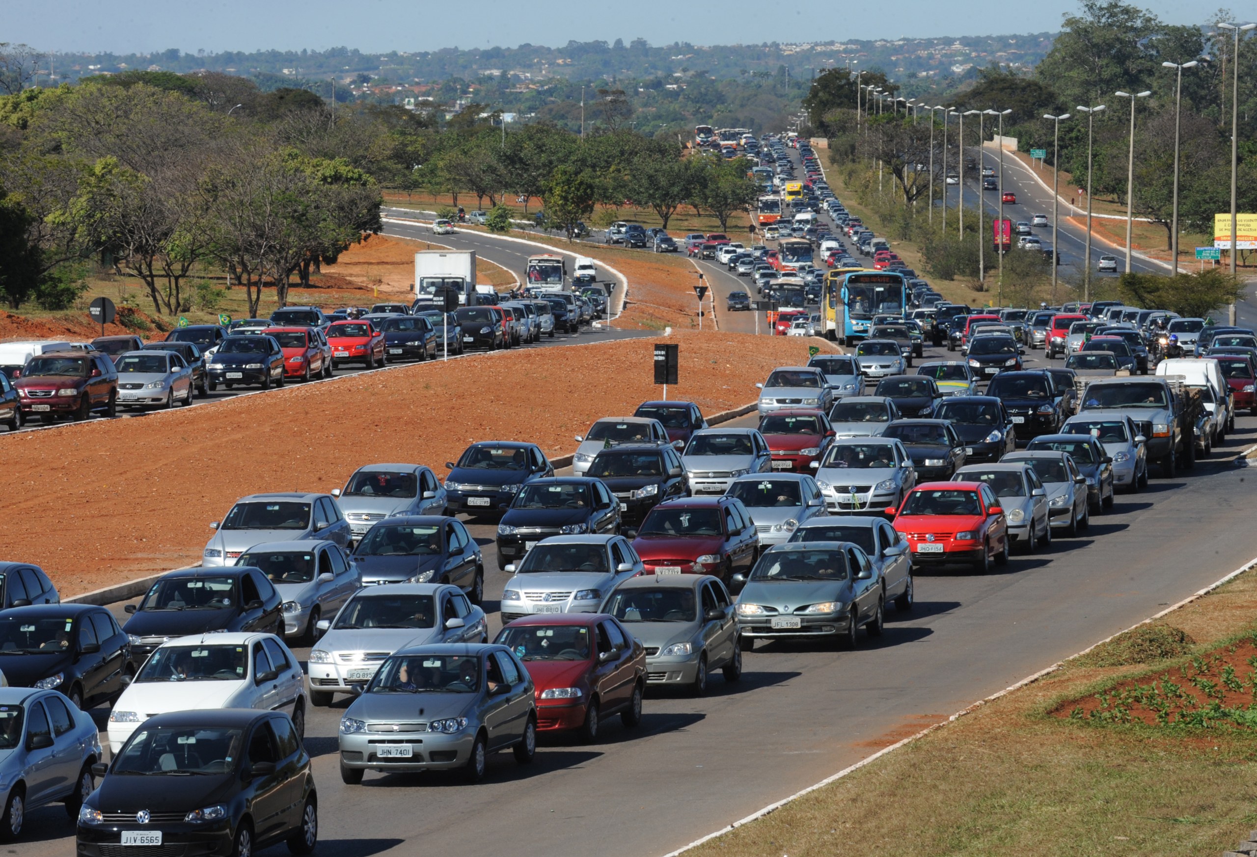 Longa fila de carros e caminhões em congestionamento em uma rodovia de pista dupla sob luz do dia.