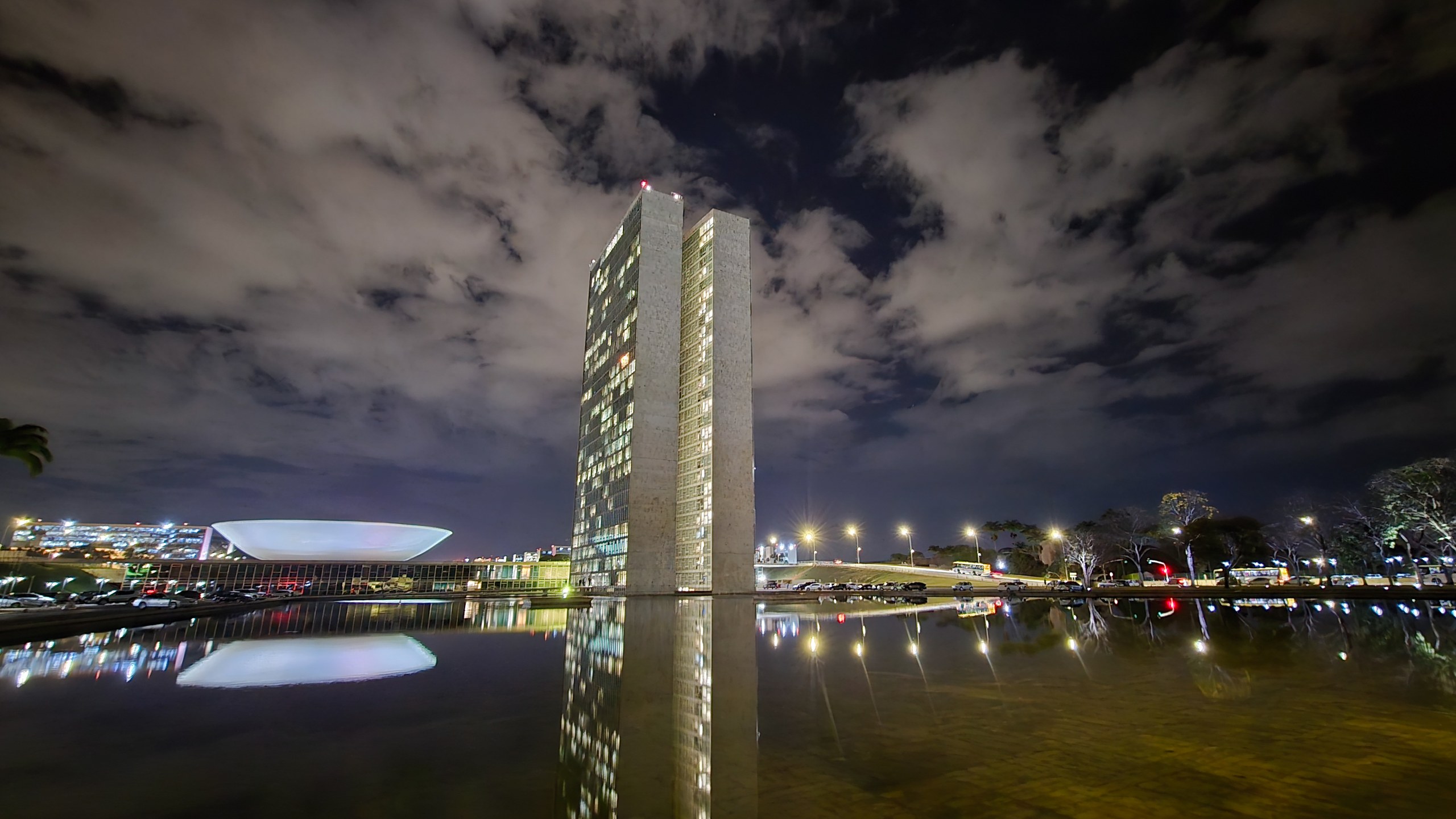 Vista noturna do Congresso Nacional em Brasília, com as torres iluminadas refletidas no espelho d'água.
