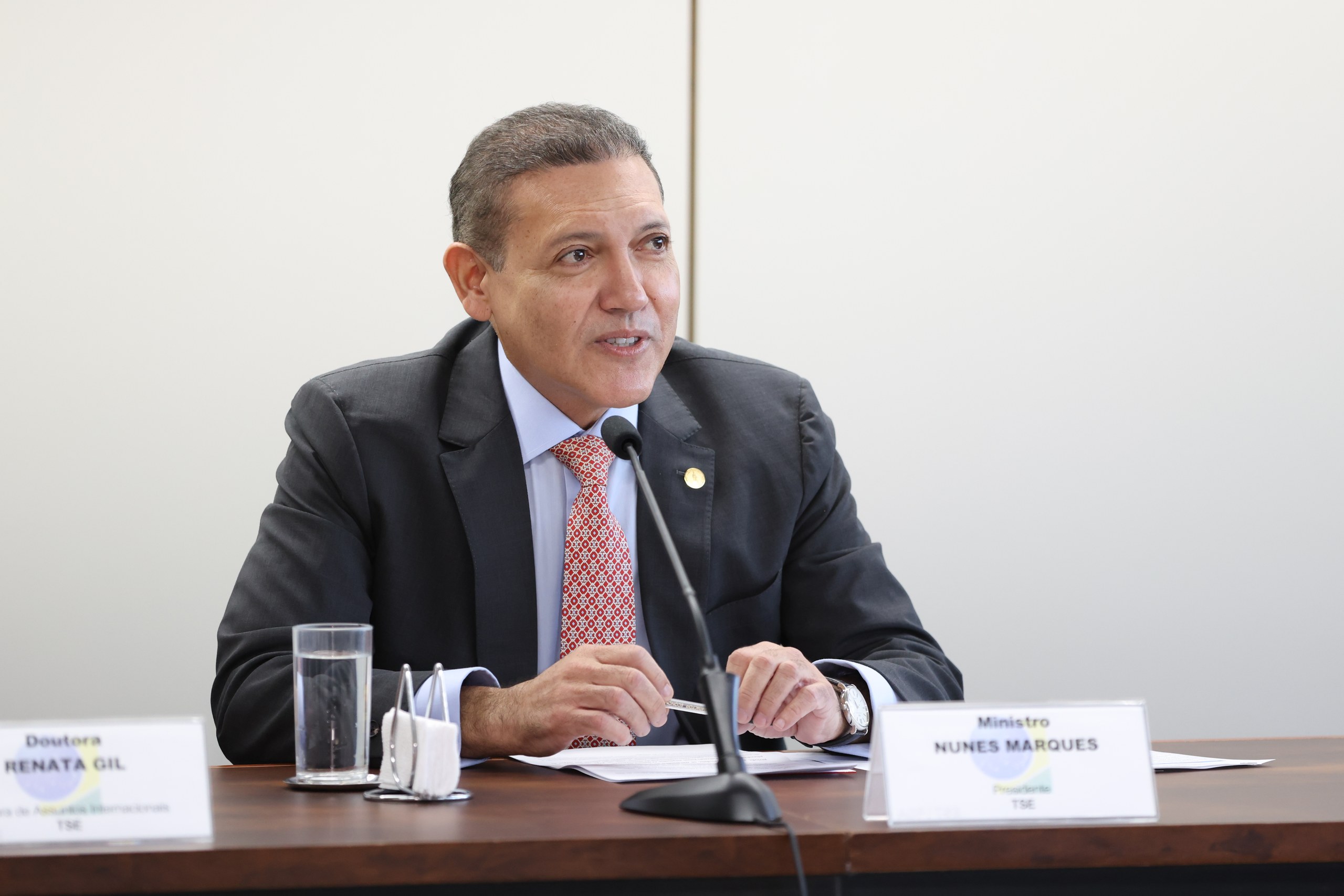 Homem de terno fala ao microfone durante evento formal com placas de identificação sobre a mesa. Na foto: Nunes Marques.
