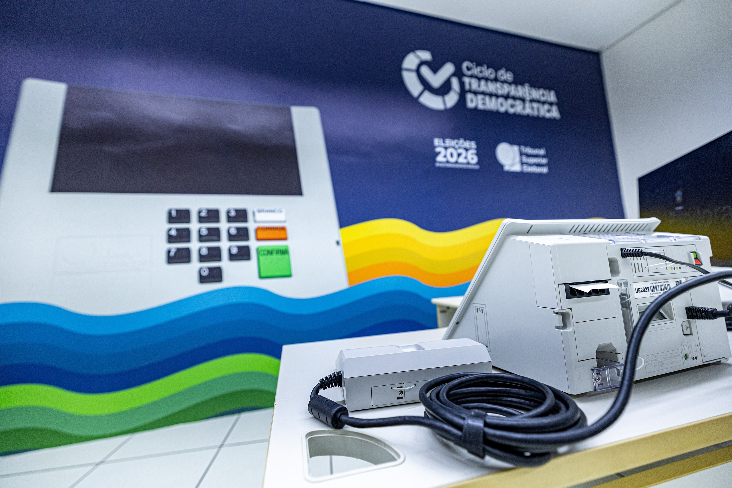Urna eletrônica brasileira exposta em evento sobre transparência democrática para as eleições de 2026.