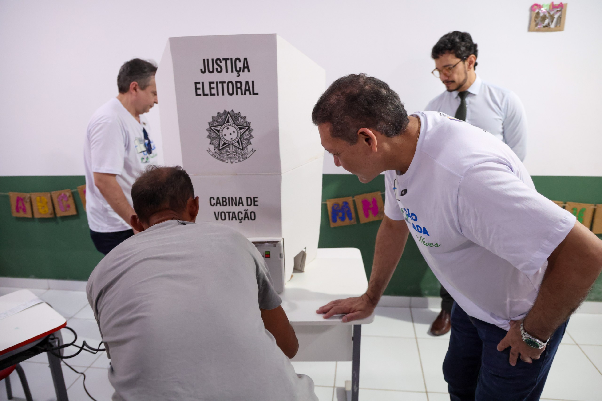 Eleitores em uma seção eleitoral brasileira ao lado de uma cabine de votação da Justiça Eleitoral.