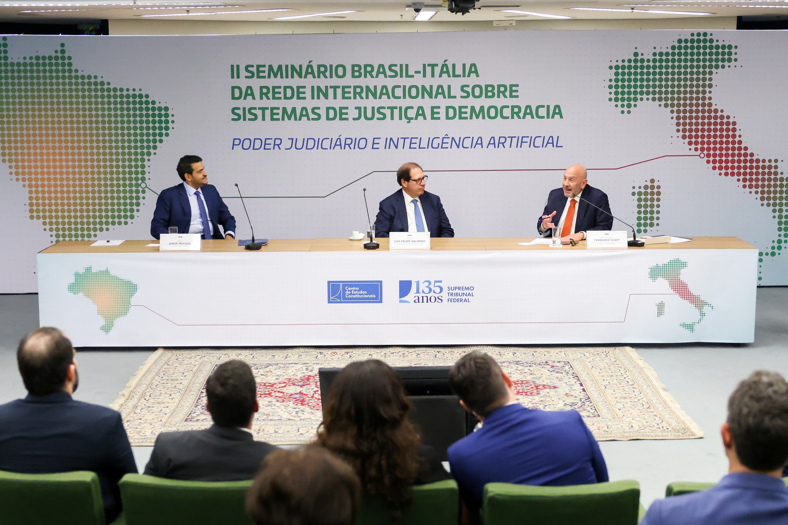Três homens sentados atrás de uma mesa com microfones durante seminário sobre sistemas de justiça e inteligência artificial em ambiente institucional. Na foto: Jorge Messias.