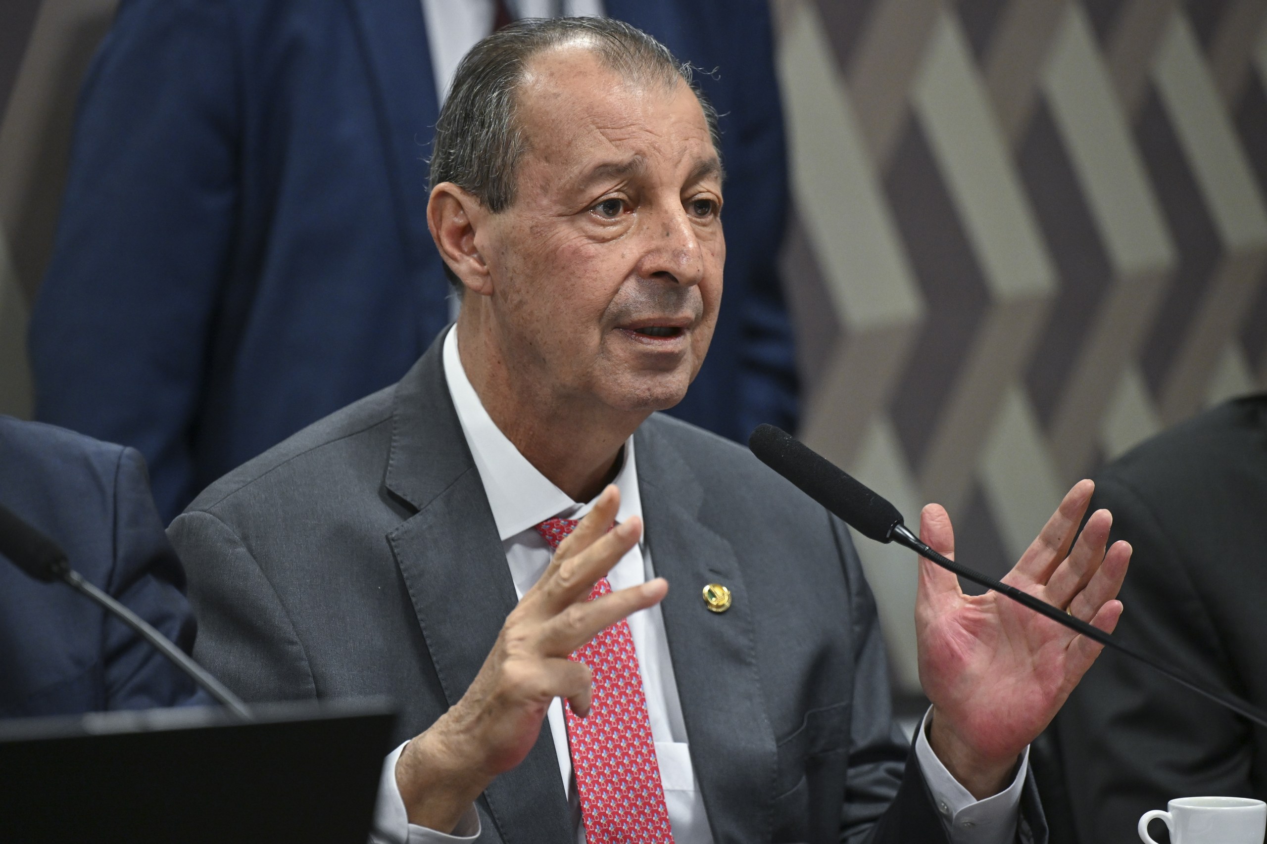 Um homem de terno e gravata gesticula com as mãos enquanto fala ao microfone em uma audiência formal. Na foto: Omar Aziz.