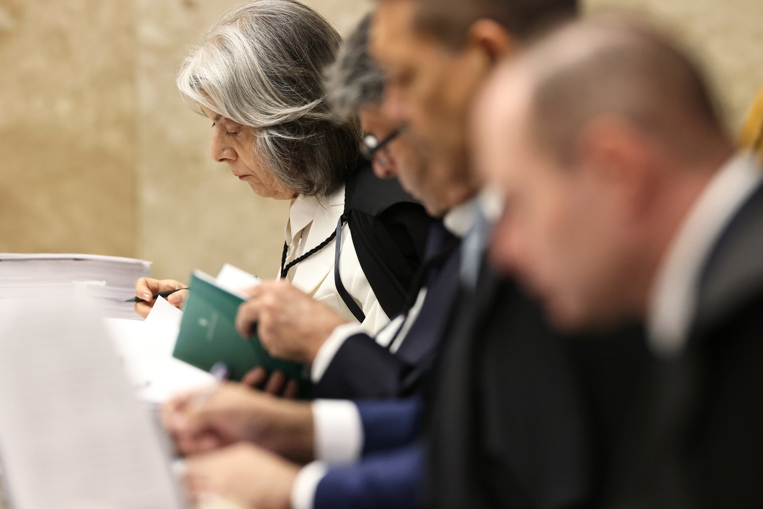 Três magistrados sentados em bancada analisam documentos e papéis durante sessão de julgamento em ambiente formal de tribunal.